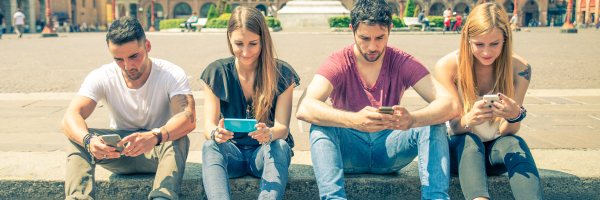 Vier jongeren zitten aan de rand van een plein op hun mobiele telefoon.