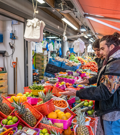 Twee bezoekers aan de Haagse Markt staan voor een stalletje met groente en fruit.