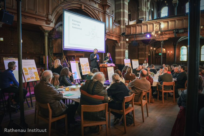 Zijaanzicht van zaal met mensen aan tafels die kijken naar wit scherm
