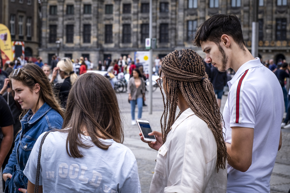 Mensen op straat in Amsterdam die op hun telefoon kijken. Coverfoto rapport initiatieven voor digitale democratie op nationaal niveau.