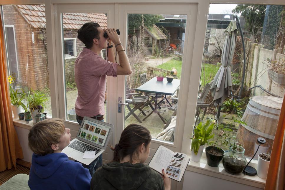 Drie jongeren tellen vanuit hun kamer de vogels in de tuin voor de Nationale Tuinvogeltelling.