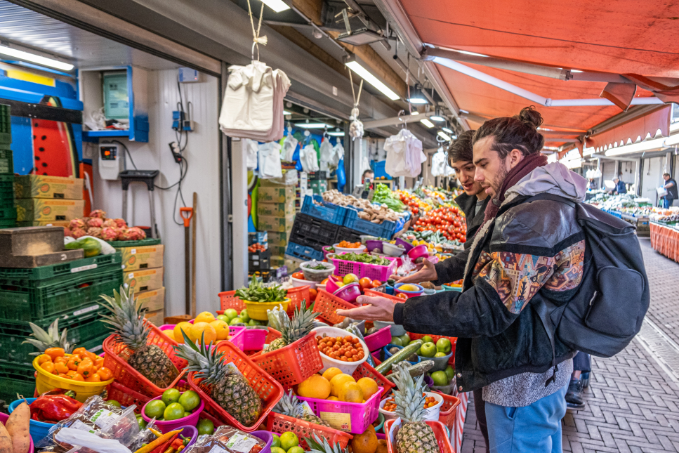 Twee bezoekers aan de Haagse Markt staan voor een stalletje met groente en fruit.