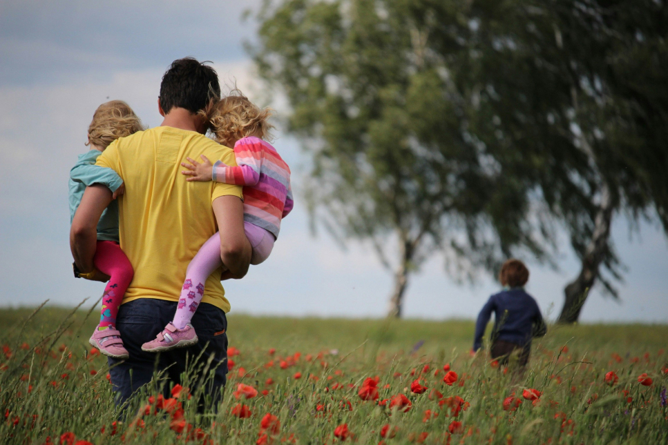 Een vader loopt met zijn kinderen door een bloemenveld