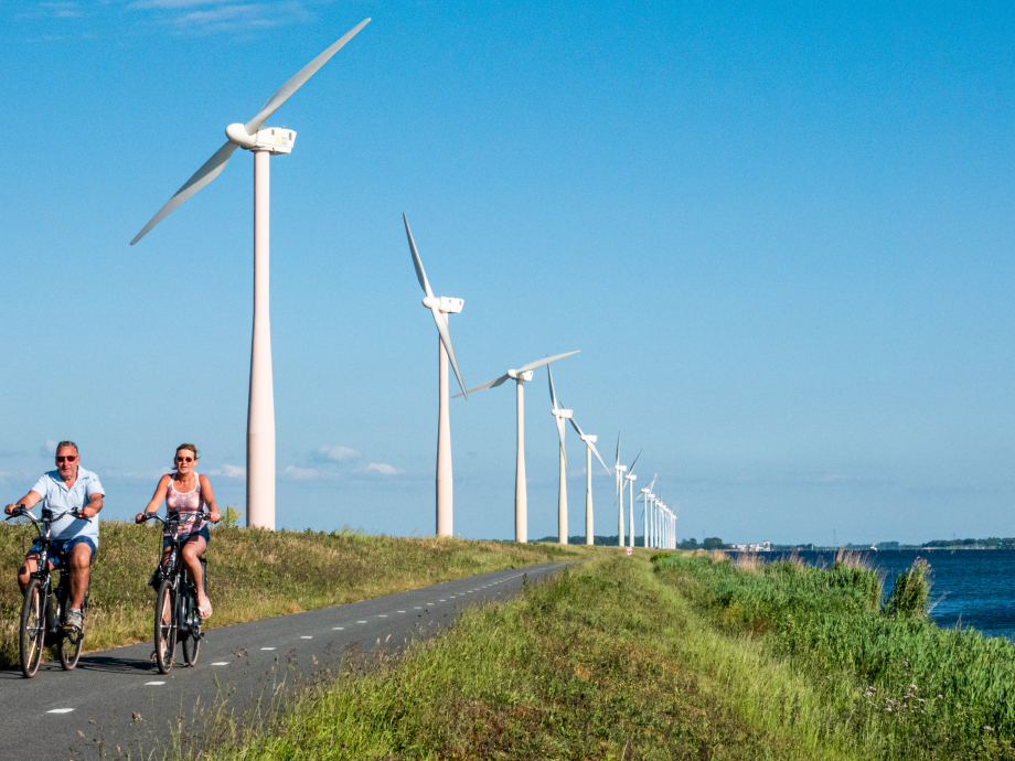 Twee mensen fietsen langs windmolens op de Eemmeerdijk