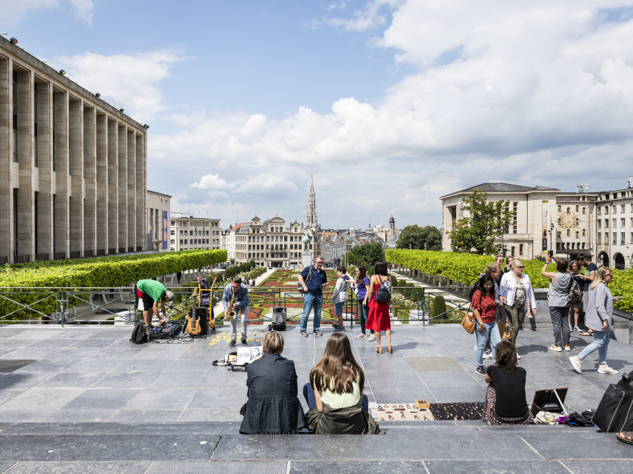 Mensen zitten bovenaan de trappen van de Kunstberg en kijken uit op het oude centrum van Brussel.
