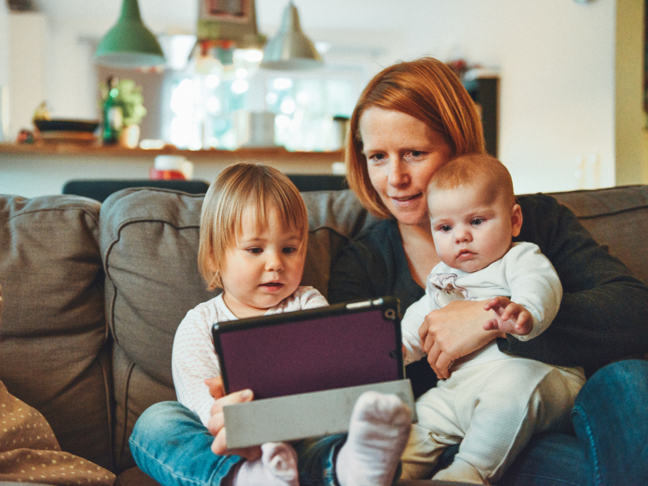 Een moeder zit met 2 kleine kinderen op de bank met een tablet
