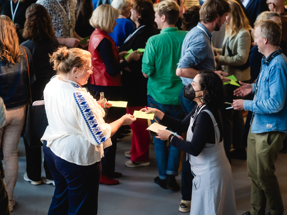 Twee deelnemers aan het macht-symposium wisselen gele briefjes uit.