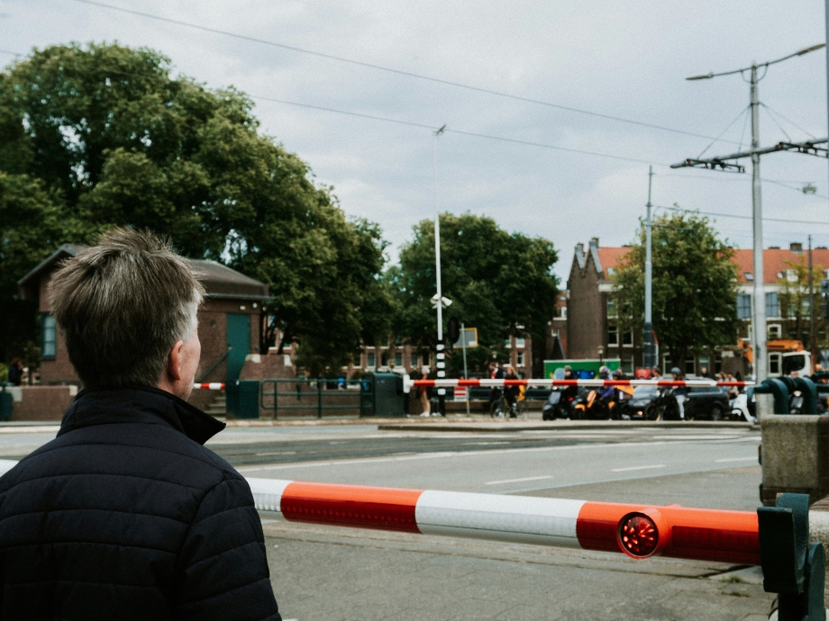 Persoon voor een slagboom die naar motorverkeer kijkt 
