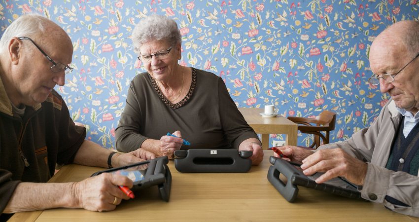 Drie oudere mensen zitten samen te werken op hun laptops