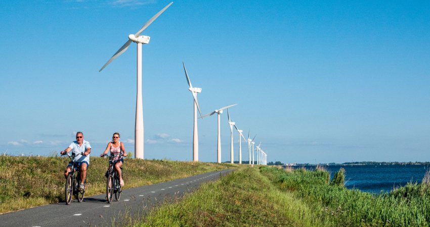 Twee mensen fietsen langs windmolens op de Eemmeerdijk