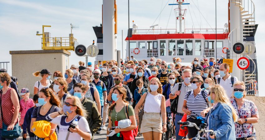 Tientallen mensen met mondkapje lopen van een veerboot af