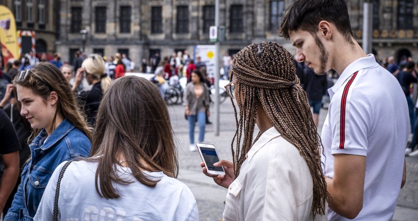 Mensen op straat in Amsterdam die op hun telefoon kijken. Coverfoto rapport initiatieven voor digitale democratie op nationaal niveau.