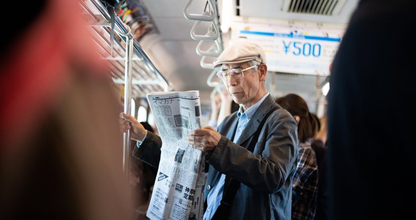 An elderly person reads the newspaper in the public transport