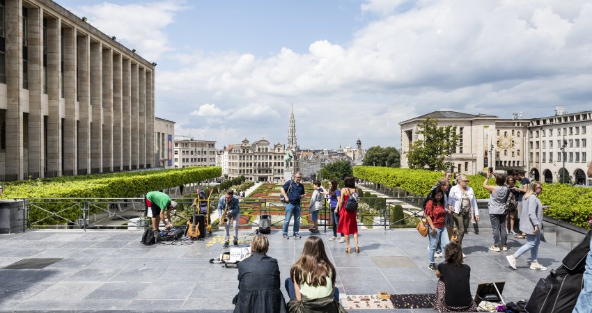 Mensen zitten bovenaan de trappen van de Kunstberg en kijken uit op het oude centrum van Brussel.
