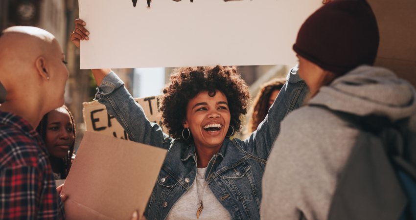 Een vrouw houdt lachend een bord omhoog met 'women."