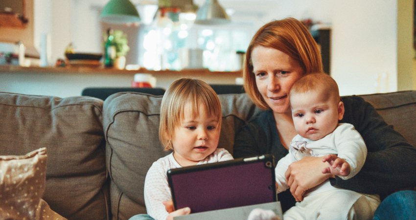 Een moeder zit met 2 kleine kinderen op de bank met een tablet