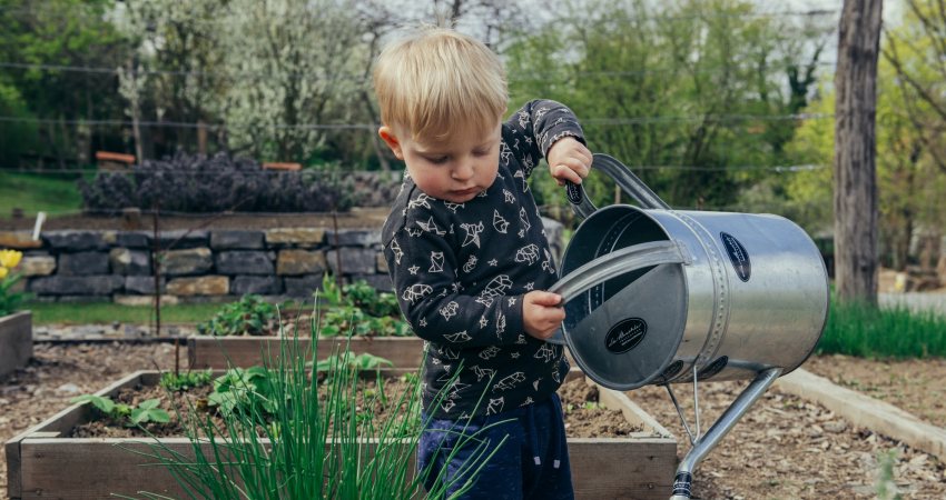 Een jongetje geeft planten water met een grote gieter