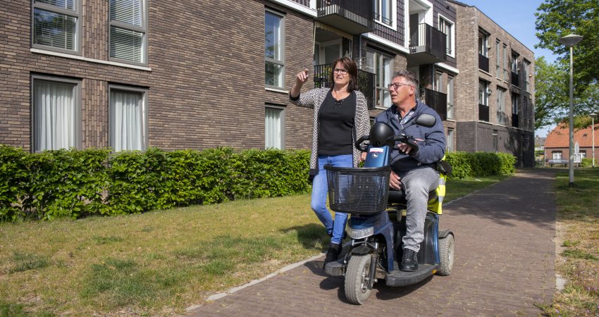 Een man op een scootmobiel is op pad met een wandelende vrouw