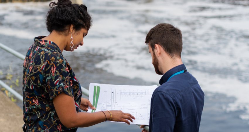 Twee wetenschappers staan naast het water voor hun onderzoek naar overstromingsmanagement