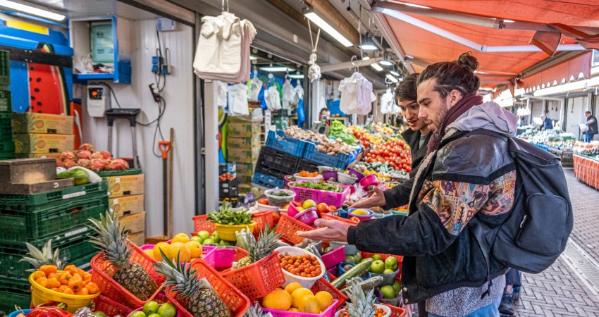 Twee bezoekers aan de Haagse Markt staan voor een stalletje met groente en fruit.