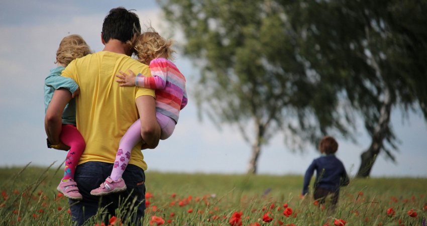 Een vader loopt met zijn kinderen door een bloemenveld