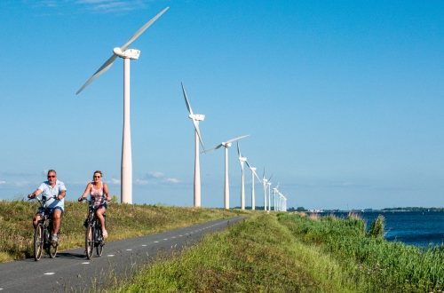 Twee mensen fietsen langs windmolens op de Eemmeerdijk