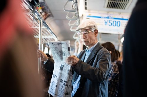 An elderly person reads the newspaper in the public transport