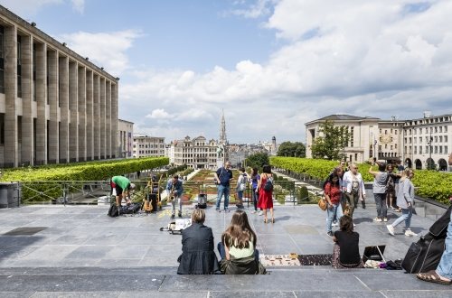 Mensen zitten bovenaan de trappen van de Kunstberg en kijken uit op het oude centrum van Brussel.