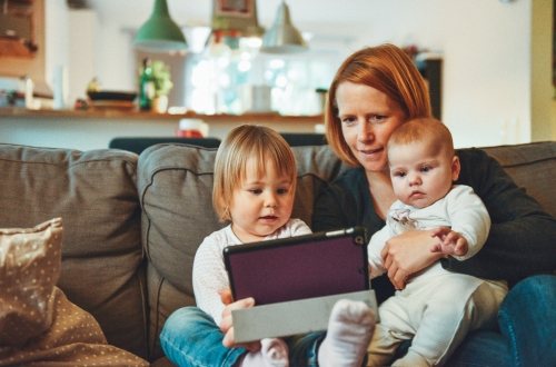 Een moeder zit met 2 kleine kinderen op de bank met een tablet