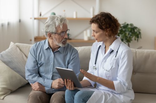 Een dokter zit op de bank met een oudere man terwijl ze bespreken wat er op een tablet staat