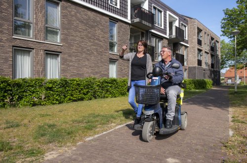 Een man op een scootmobiel is op pad met een wandelende vrouw