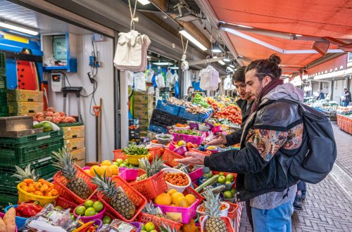 Twee bezoekers aan de Haagse Markt staan voor een stalletje met groente en fruit.