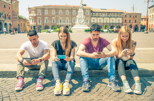 Vier jongeren zitten aan de rand van een plein op hun mobiele telefoon.
