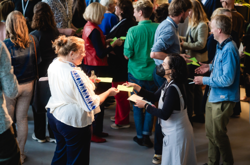 Twee deelnemers aan het macht-symposium wisselen gele briefjes uit.