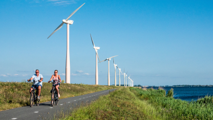 Twee mensen fietsen langs windmolens op de Eemmeerdijk