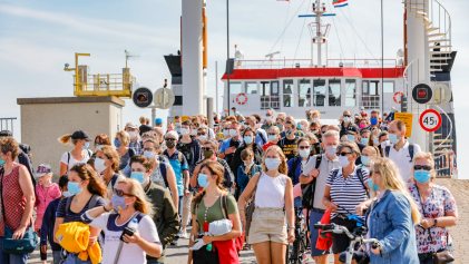 Tientallen mensen met mondkapje lopen van een veerboot af