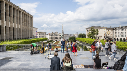 Mensen zitten bovenaan de trappen van de Kunstberg en kijken uit op het oude centrum van Brussel.