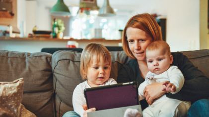 Een moeder zit met 2 kleine kinderen op de bank met een tablet
