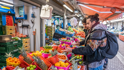 Twee bezoekers aan de Haagse Markt staan voor een stalletje met groente en fruit.