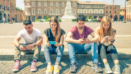 Vier jongeren zitten aan de rand van een plein op hun mobiele telefoon.