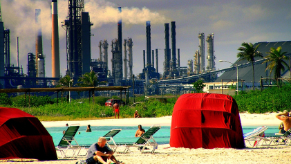 Mensen op een strand op Aruba met op de achtergrond een olierafinaderij