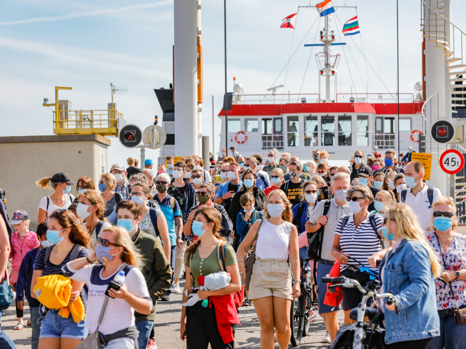 Tientallen mensen met mondkapje lopen van een veerboot af