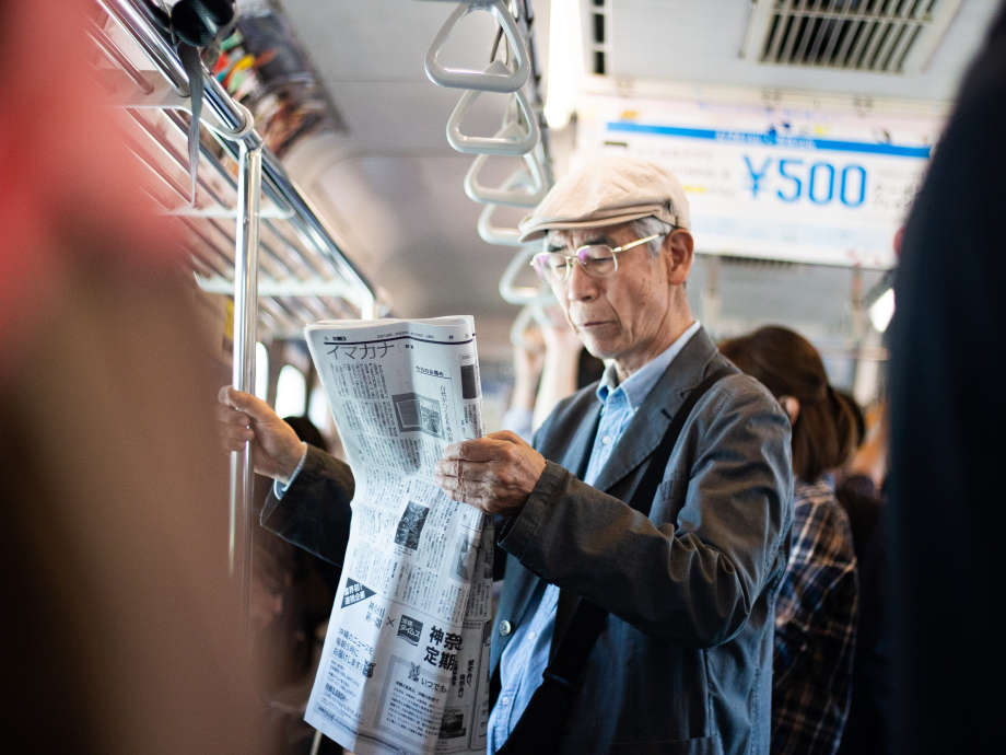 An elderly person reads the newspaper in the public transport