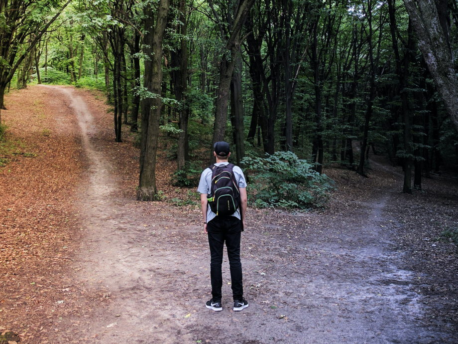 Een man staat in het bos en moet kiezen of hij links of rechts het bospad volgt