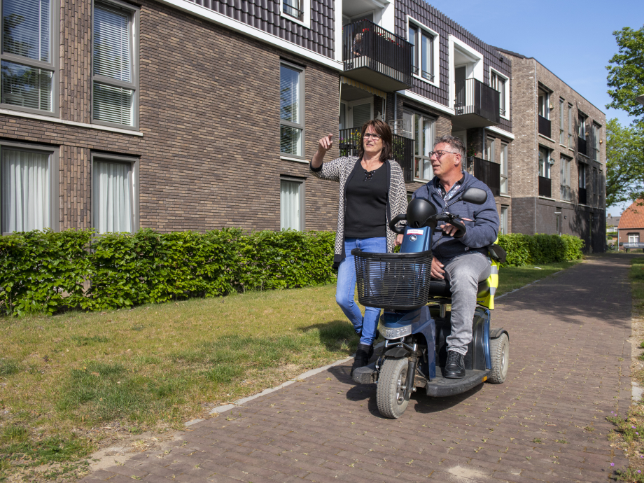 Een man op een scootmobiel is op pad met een wandelende vrouw