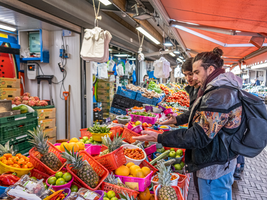 Twee bezoekers aan de Haagse Markt staan voor een stalletje met groente en fruit.