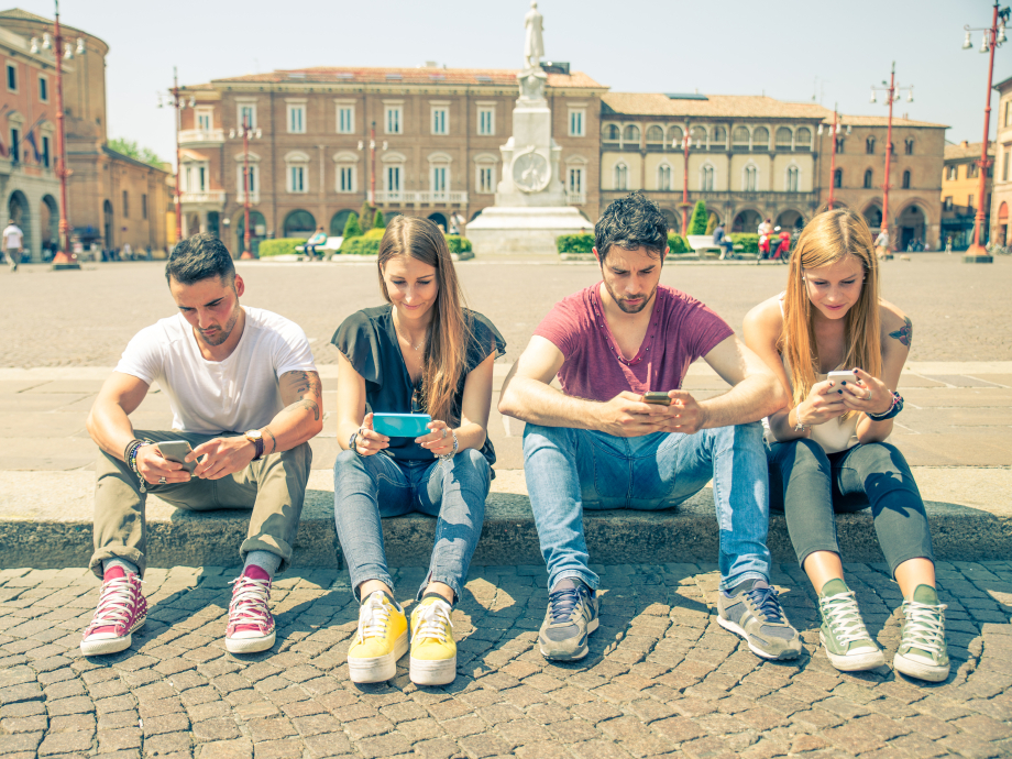 Vier jongeren zitten aan de rand van een plein op hun mobiele telefoon.