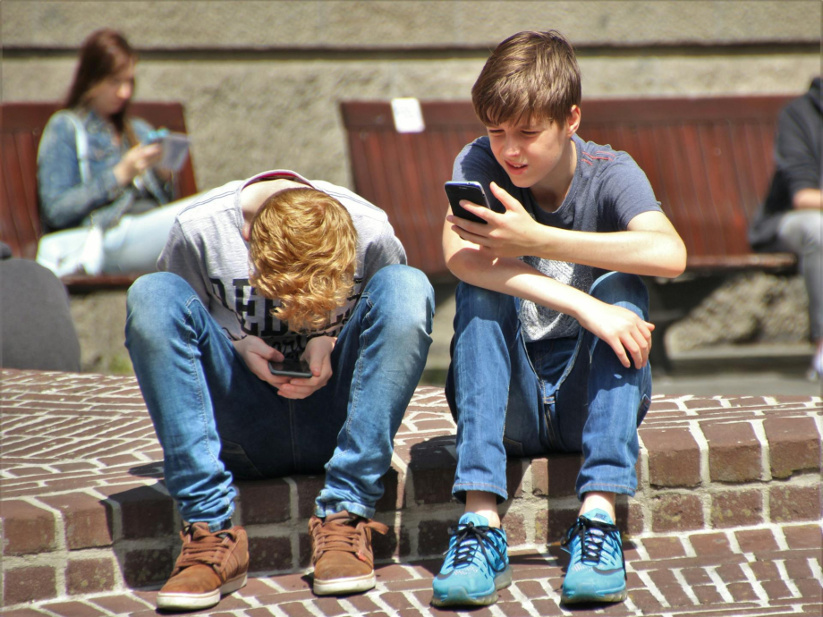 Twee jongens zitten buiten en kijken op hun telefoon