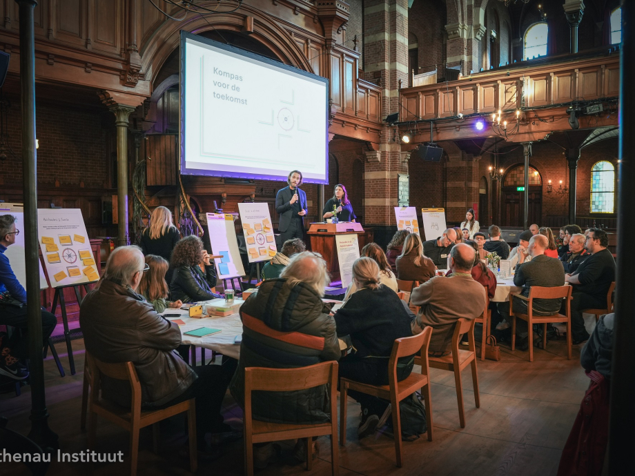 Zijaanzicht van zaal met mensen aan tafels die kijken naar wit scherm