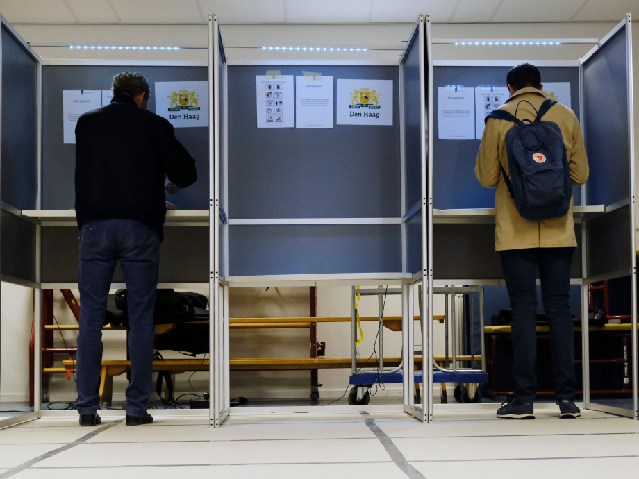 Mensen aan het stemmen in een stemhokje, gezien vanaf de rug
